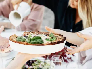 A close-up of hands passing a freshly baked quiche